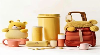 黄油小熊生活周边产品展示，包含马克杯、手机壳、帆布袋、抱枕等日用品，以奶油色和砖红色为主题色，摆放在温馨的家居场景中